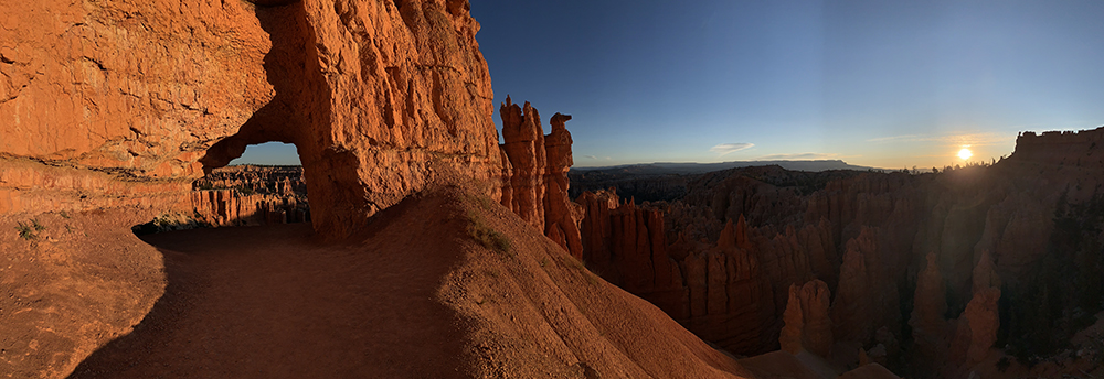 the sun rises to illuminate the red walls of bryce as the trail passes through a tunnel