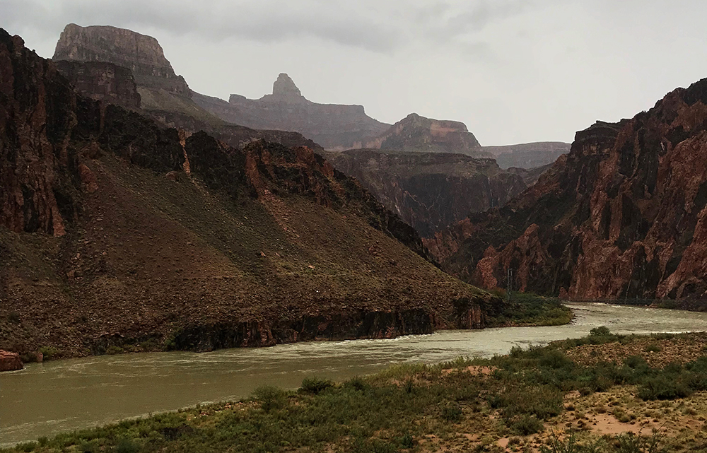 Hazy cliffs rise above the green waters of the Colorado River in a rare desert rain