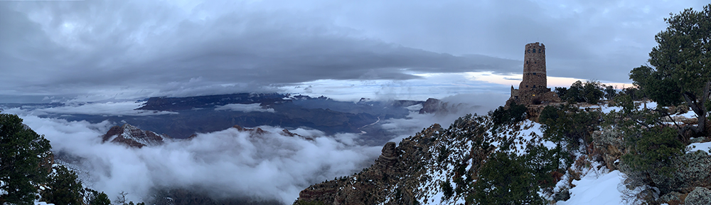 the desert view watchtower looks out over a sea of clouds as the snows of winter grace the jagged landscape of the grand canyon