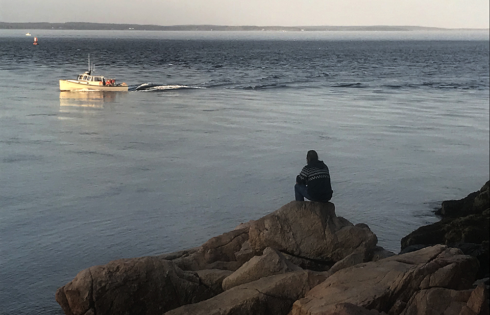 a man looks out from shore toward a boat at sunrise