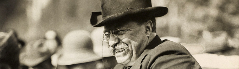 Theodore Roosevelt smiles in hat and glasses